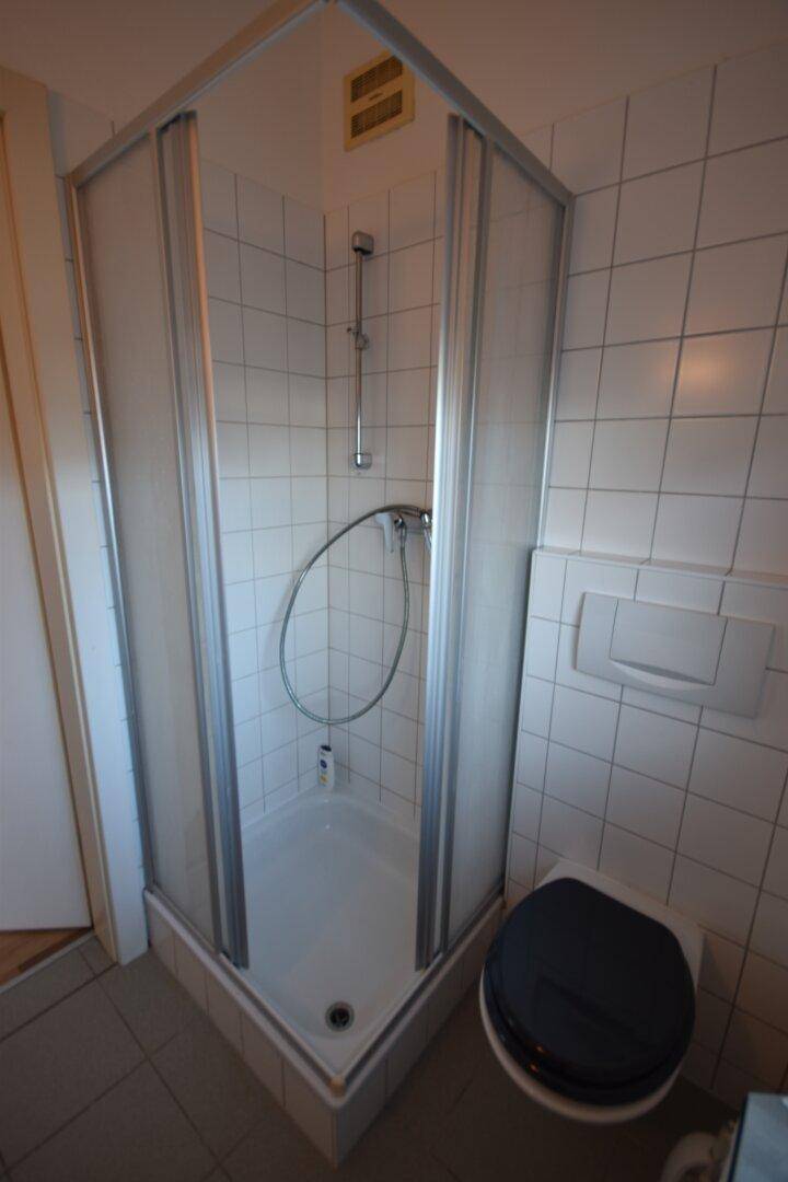 Badezimmer mit Duschkabine, Toilette und durchgehend weißen Wandfliesen.