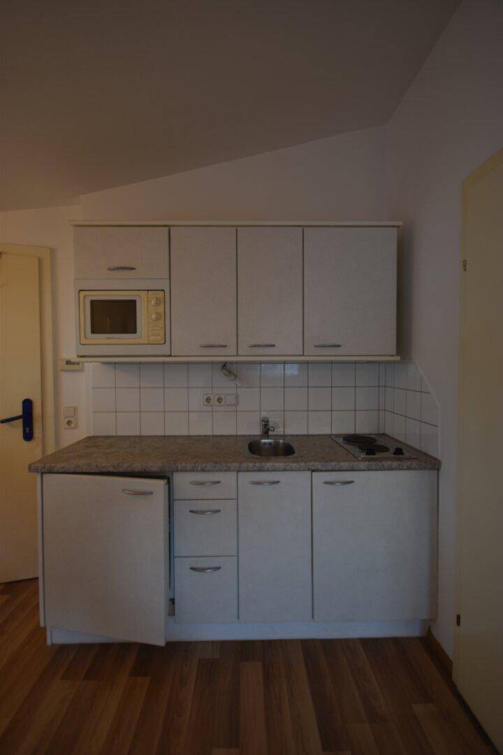 Kompakte Küchenzeile mit weißen Schränken, Fliesenrückwand, Spüle und integrierter Mikrowelle.