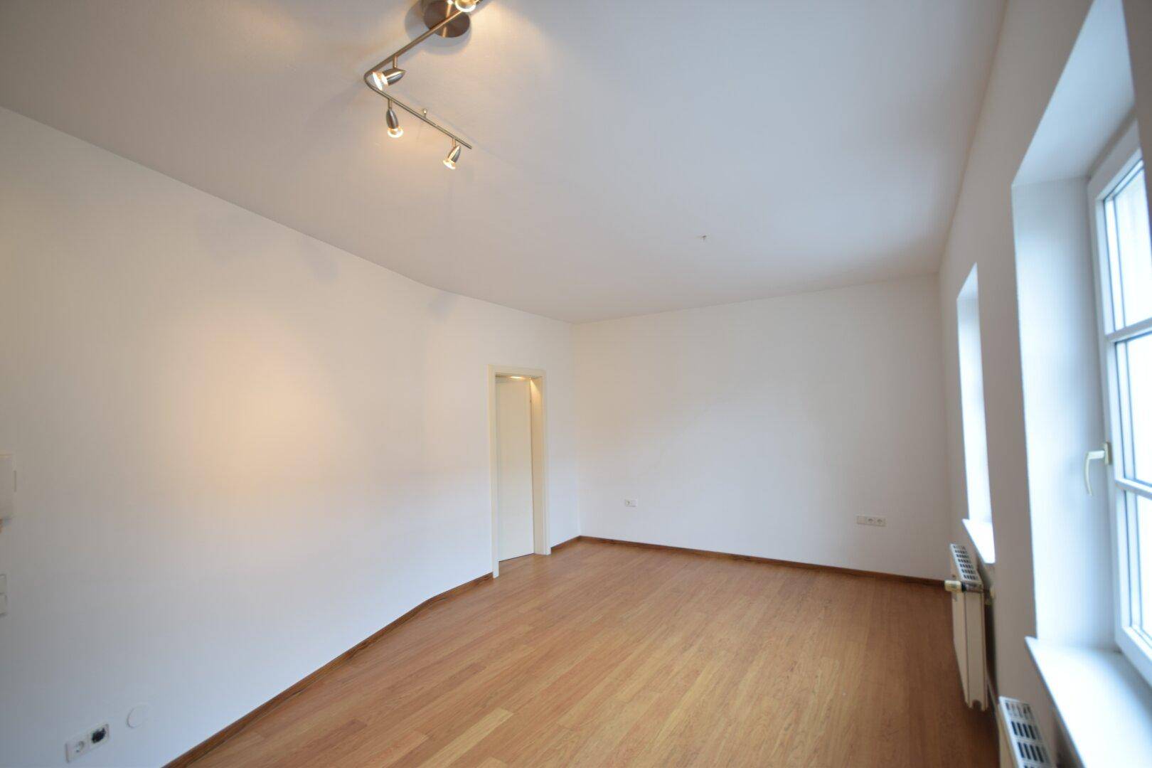Lichtdurchfluteter Wohnraum mit Holzboden und schlichten weißen Wänden.