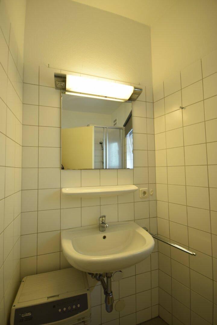 Badezimmer mit weißen Fliesen, Waschbecken, Spiegel und einer Waschmaschine.