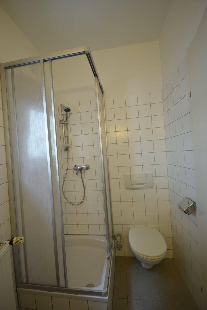 Funktionales Badezimmer mit Duschkabine, weißen Fliesen und wandhängendem WC.