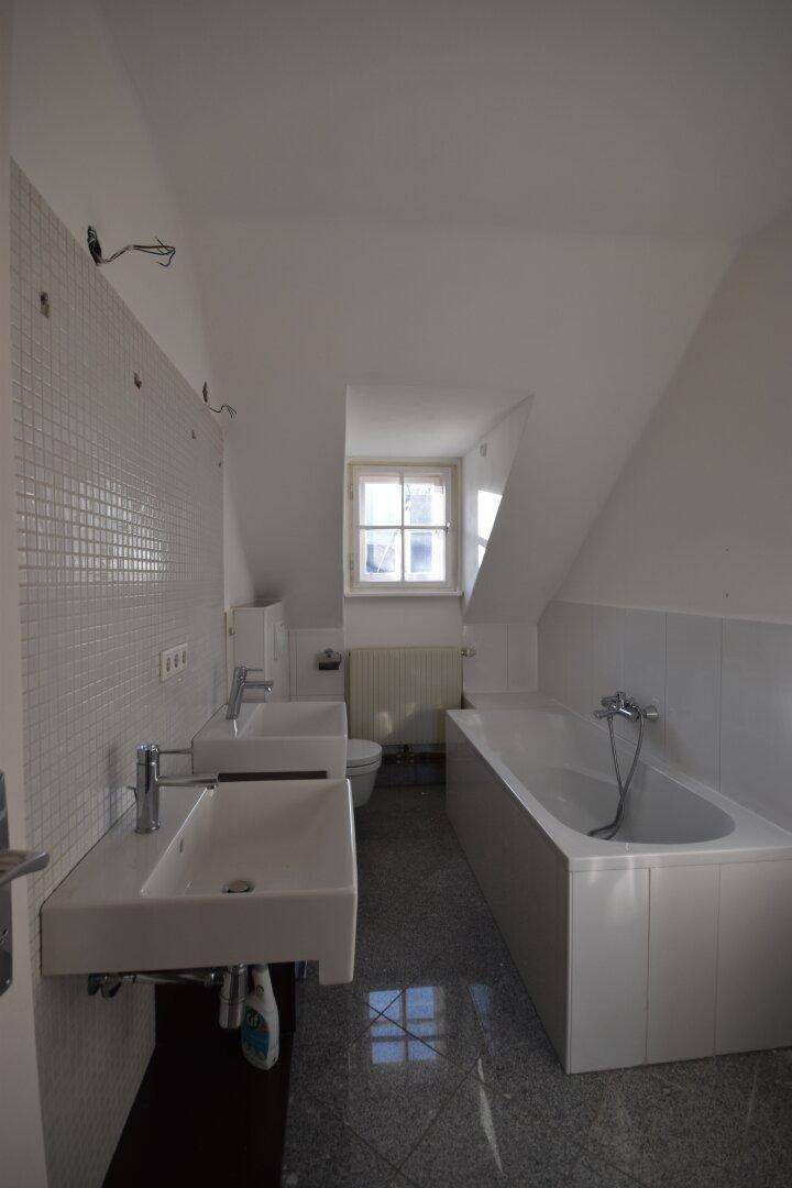 Badezimmer im Dachgeschoss mit Badewanne, Doppelwaschbecken und Mosaikfliesen.