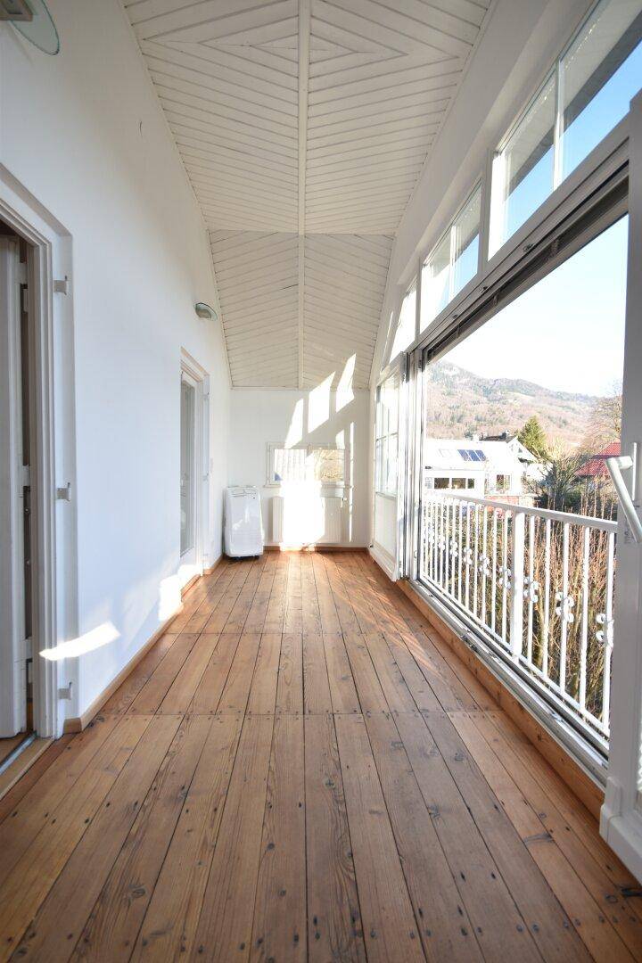 Helle, verglaste Loggia mit Holzdielenboden und weitem Blick auf die Berge.