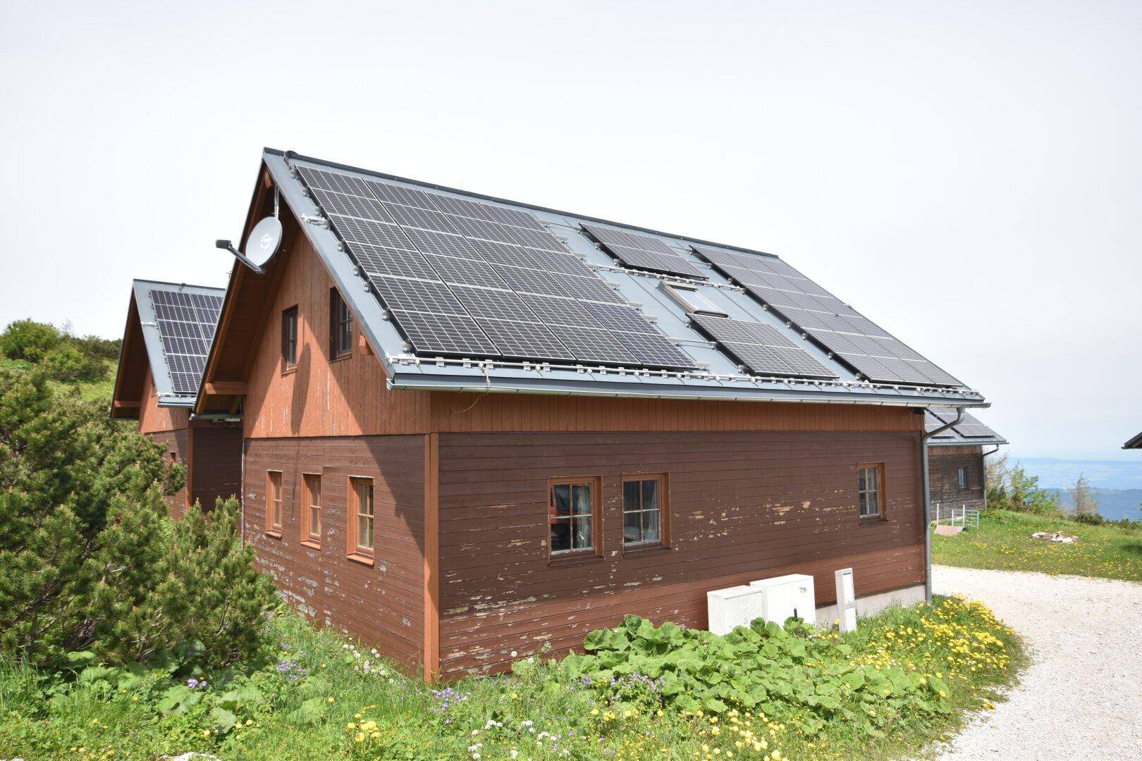 Holzhaus mit Photovoltaikanlage auf dem Dach und grüner Wiese im Vordergrund.