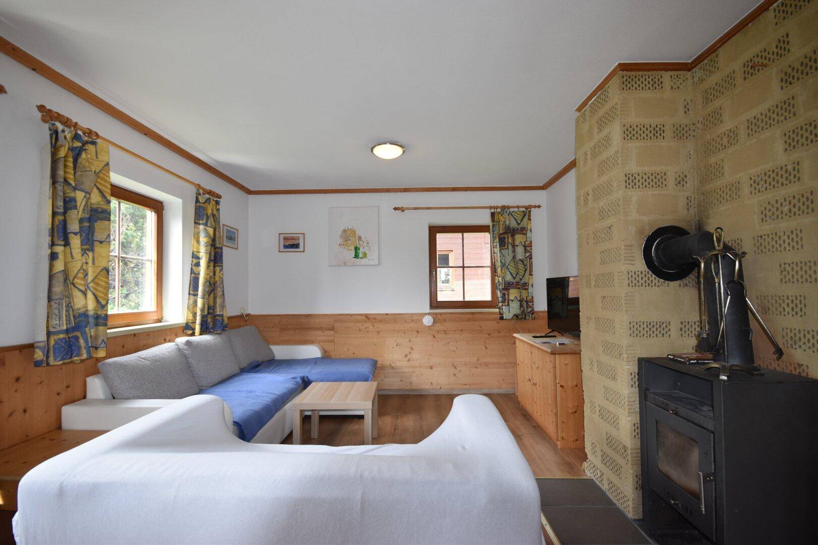 Wohnzimmer mit Kaminofen, Holzvertäfelung und bequemen Sofas in alpiner Atmosphäre.