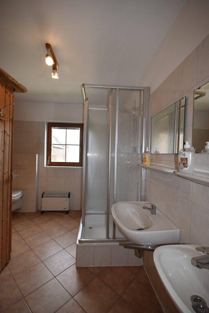 Helles Badezimmer mit Dusche, Fliesenboden und Holzvertäfelung im Landhausstil.