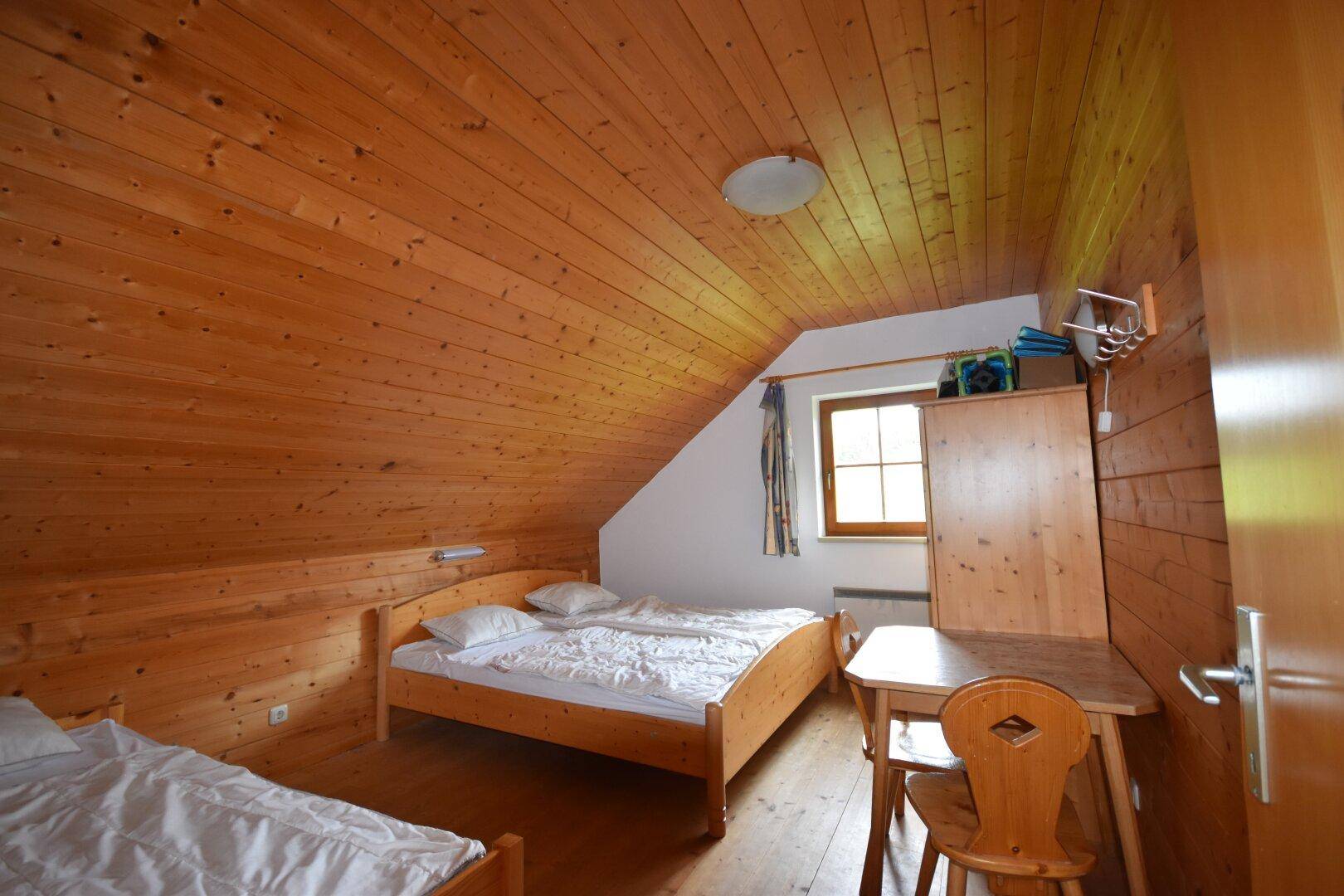 Schlafzimmer mit Holzwänden, Dachschräge und zwei Einzelbetten in rustikalem Stil.