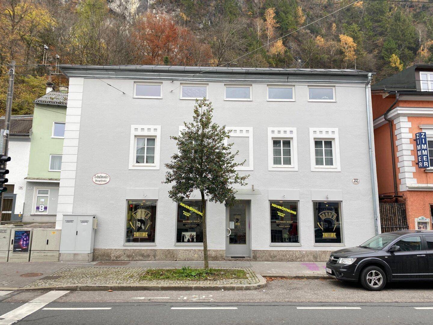 Vorderansicht eines renovierten Gebäudes mit grauer Fassade, weißen Fenstern und Geschäftseinheiten im Erdgeschoss.