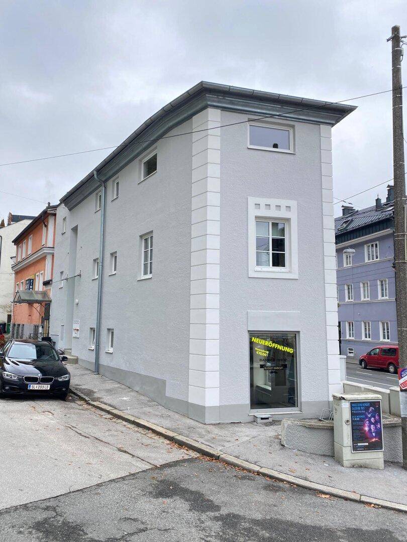 Seitenansicht des renovierten Gebäudes mit grauer Fassade, weißen Fensterrahmen und Blick auf die Straße.