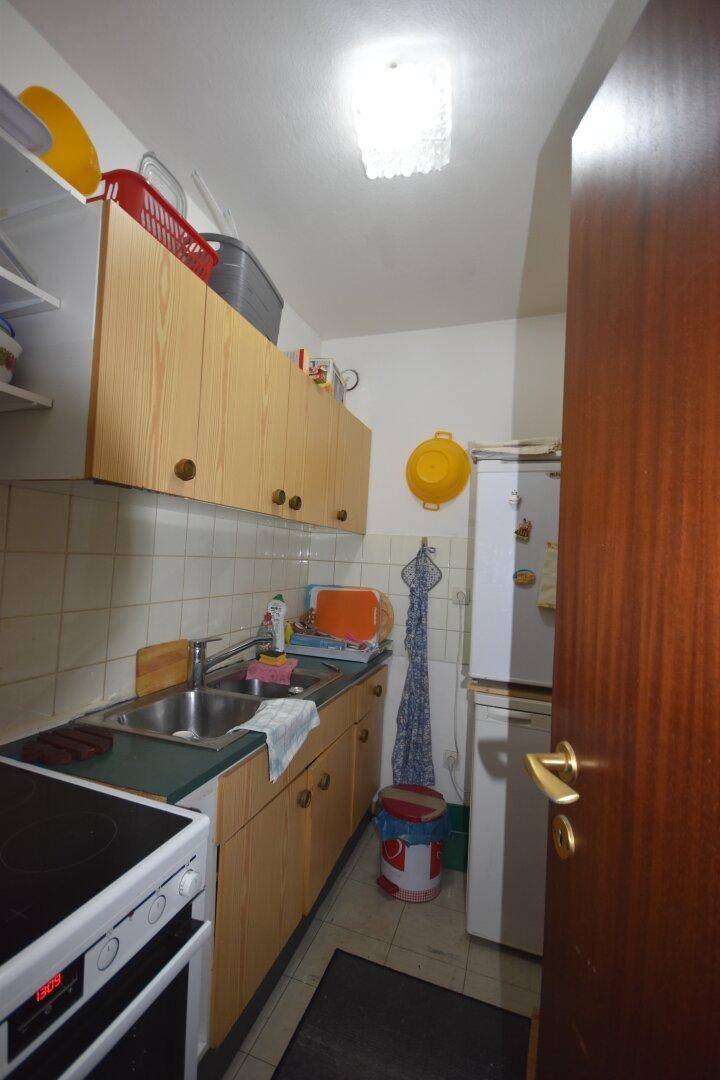 Kleine Küche mit Holzschränken, Doppelspüle und weiß gefliestem Spritzschutz.