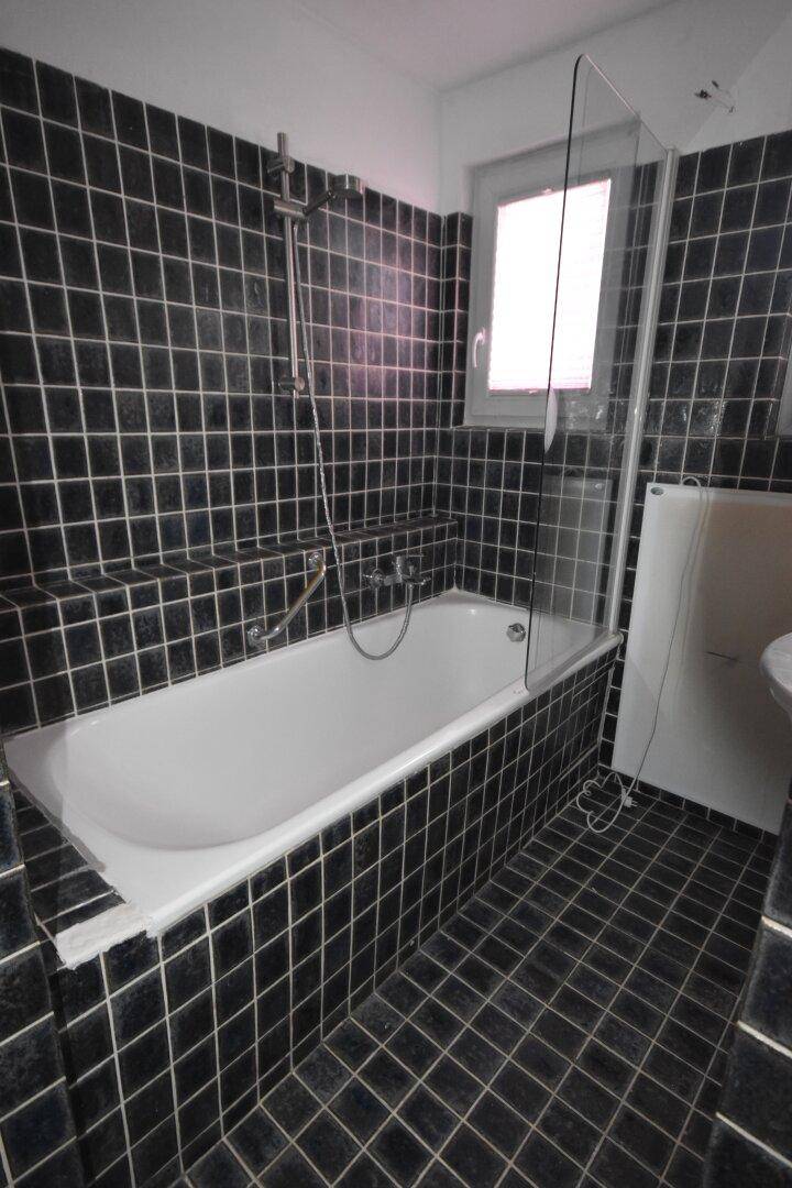 Badezimmer mit schwarzen Fliesen, Badewanne mit Duschfunktion und Fenster.