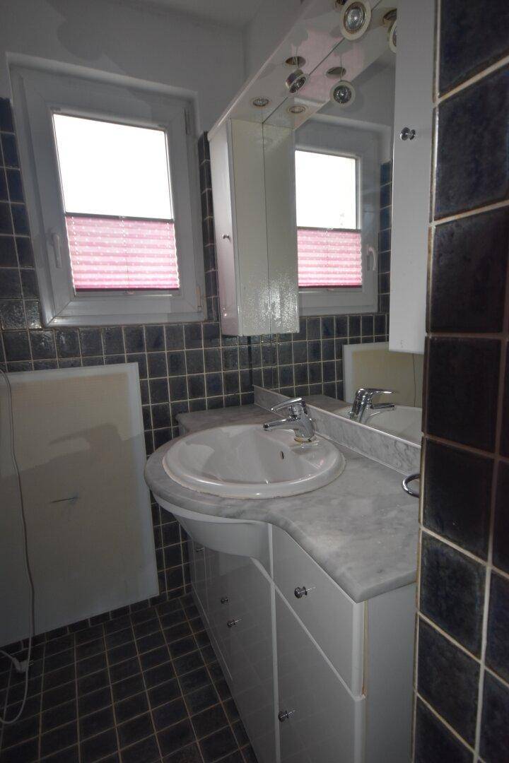 Badezimmer mit Waschtisch, Spiegelschrank und zwei Fenstern für Tageslicht.