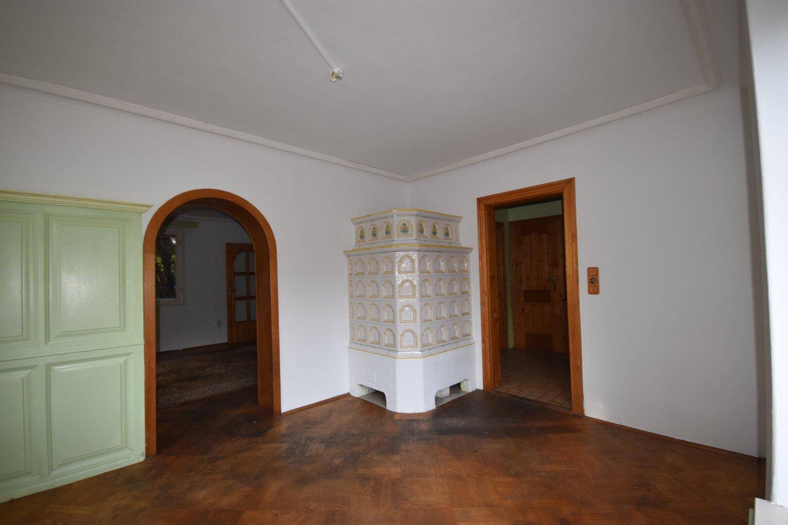 Wohnraum mit traditionellem Kachelofen, Holzboden und Holztüren zu angrenzenden Zimmern.