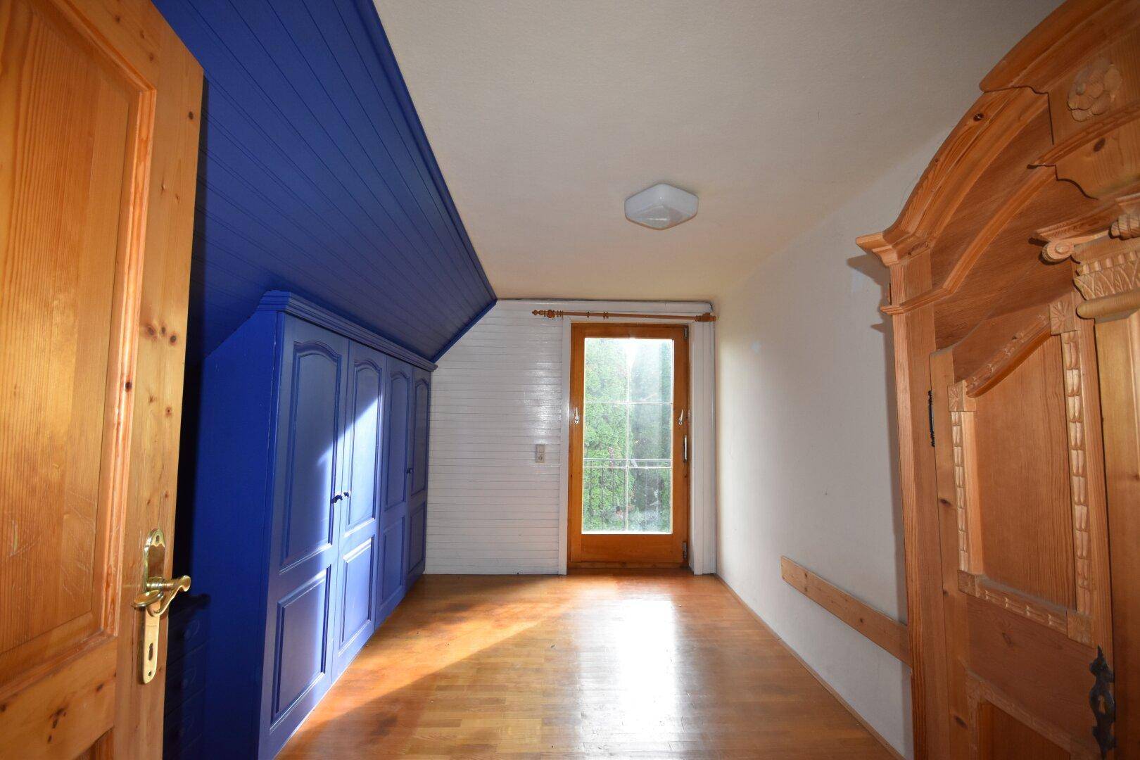 Schlafzimmer im Dachgeschoss mit blauer Holzdecke, Einbauschränken und Holzboden.