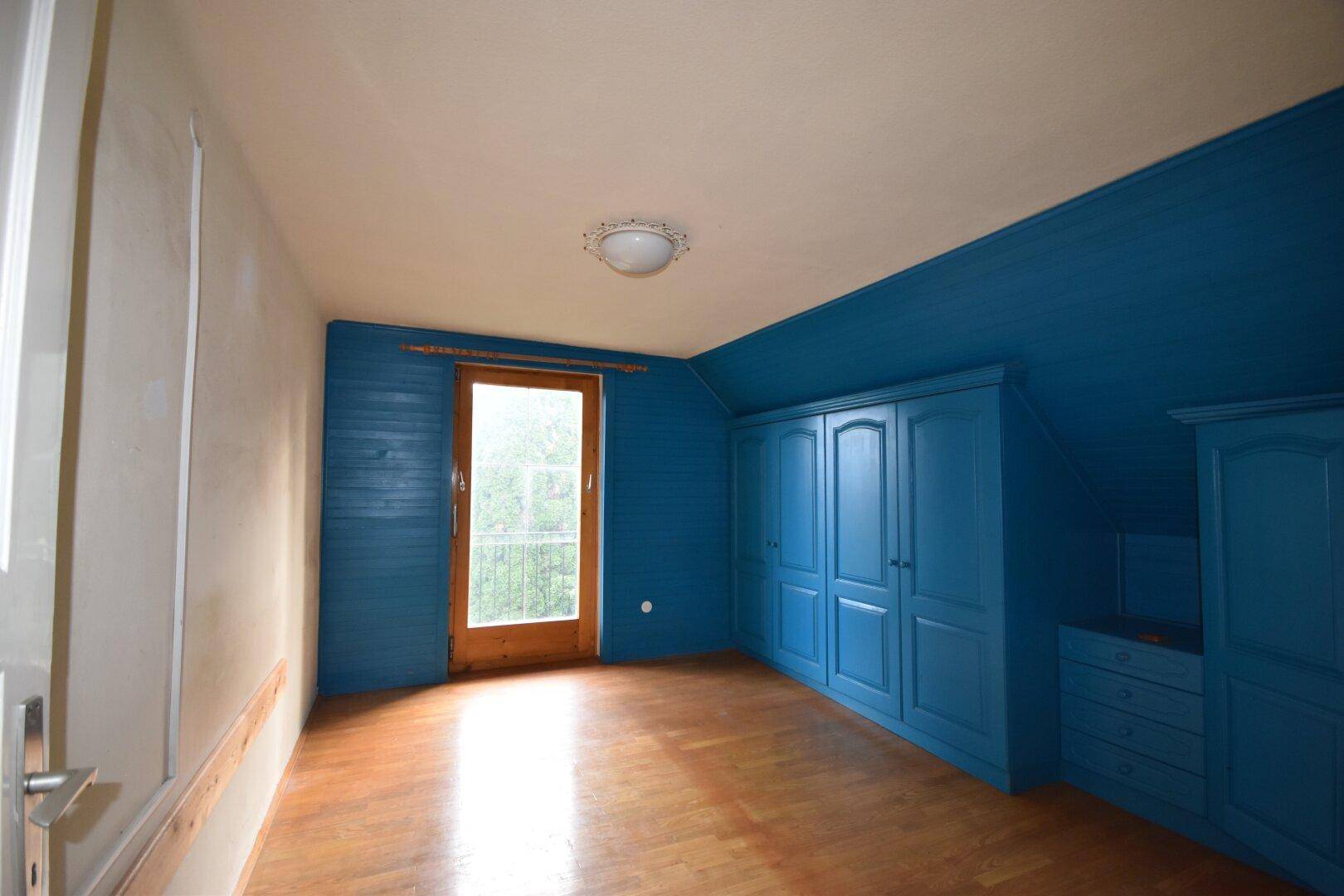 Dachgeschoss-Schlafzimmer mit blauen Einbauschränken, Holzboden und Zugang zu einem französischen Balkon.