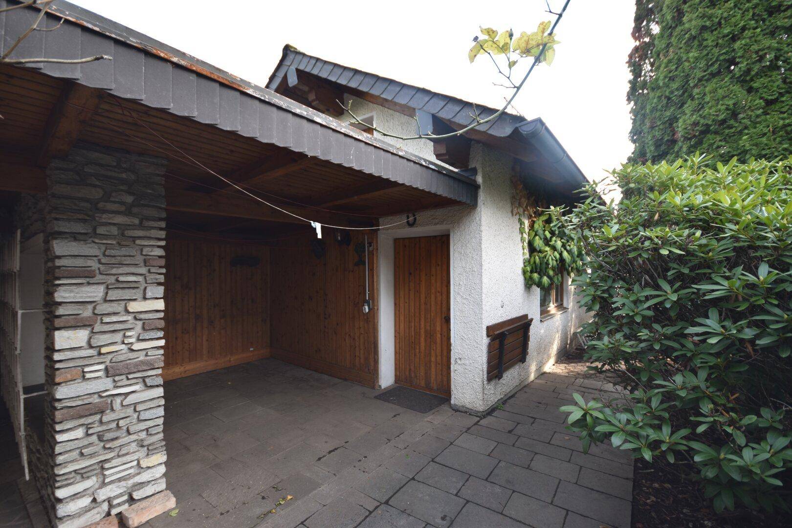 Überdachter Carport mit Steinmauer und Holzelementen neben dem Hauseingang.