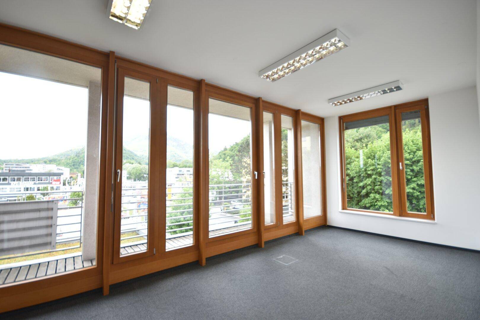Büro mit Teppichboden, breiter Fensterfront, Balkonzugang und einem weiten Stadtblick.