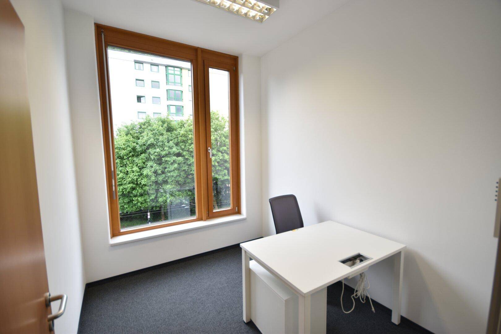 Kleines Einzelbüro mit Schreibtisch, Stuhl und einem großen Fenster mit Blick ins Grüne.