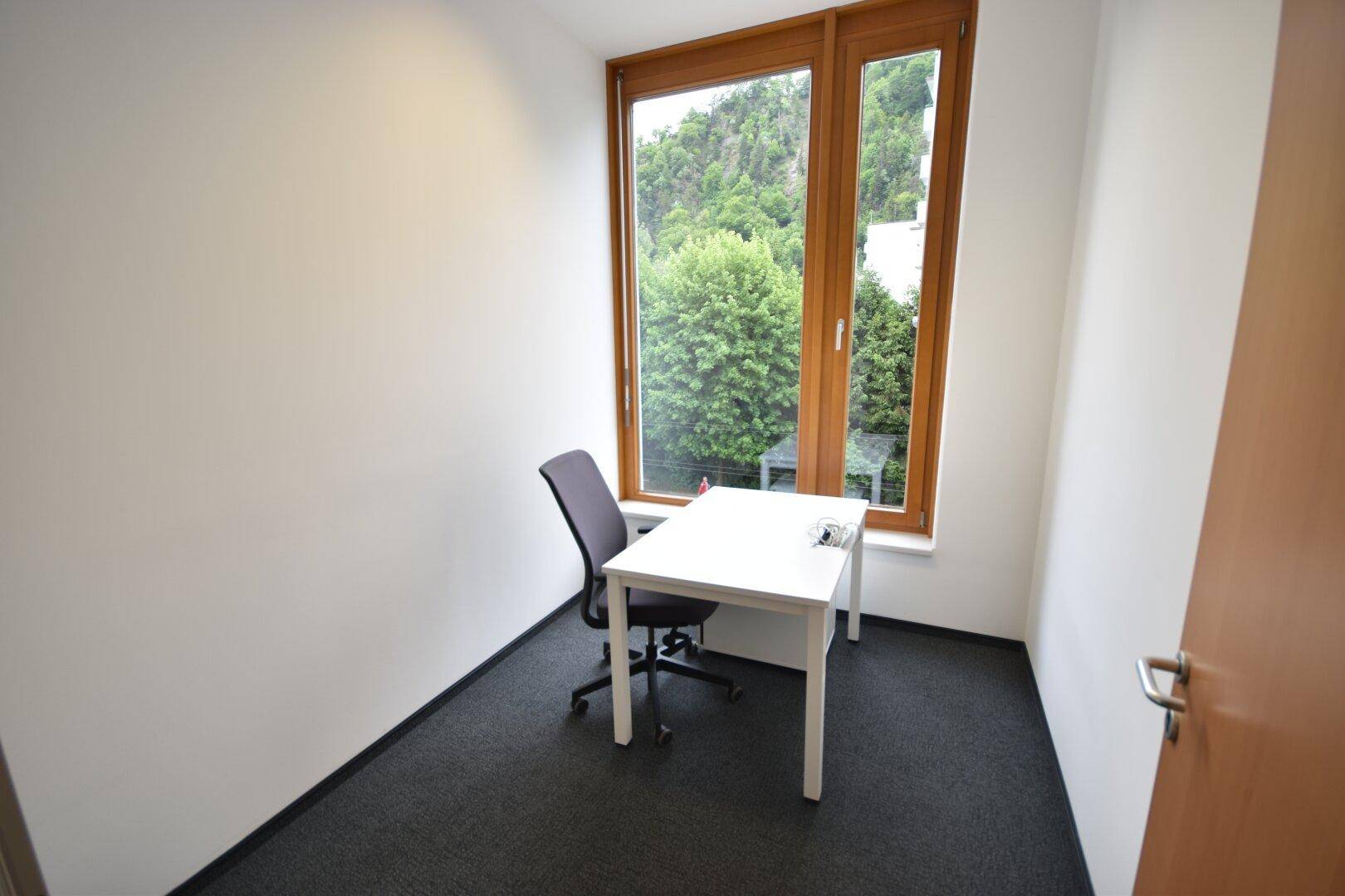 Einzelbüro mit Schreibtisch, Bürostuhl und großem Fenster, das viel Tageslicht hereinlässt.