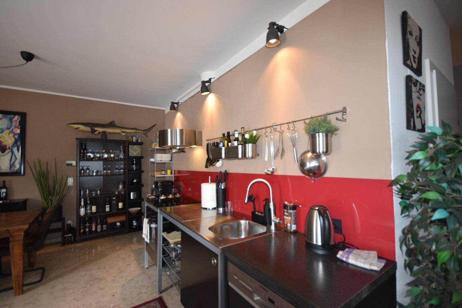 Moderne Küche mit Edelstahlgeräten, roter Spritzschutzwand und praktischen Wandhalterungen.