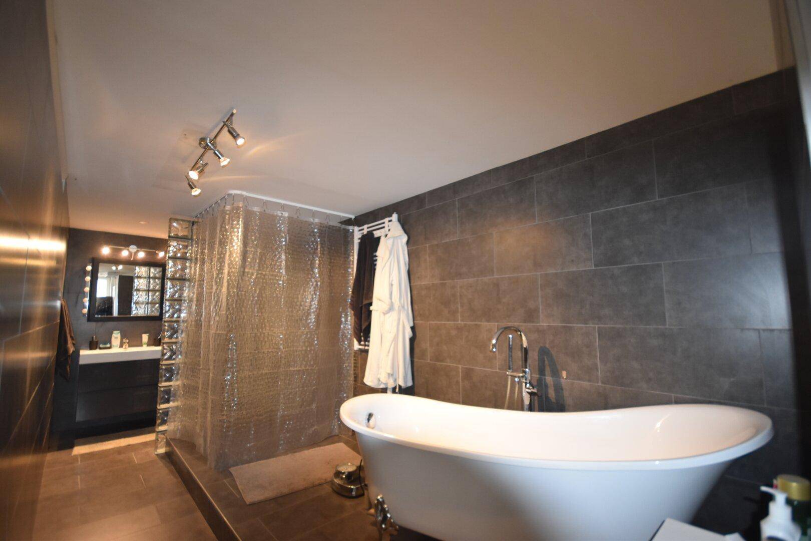 Modernes Badezimmer mit freistehender Badewanne, dunklen Fliesen und Glasbaustein-Duschwand.
