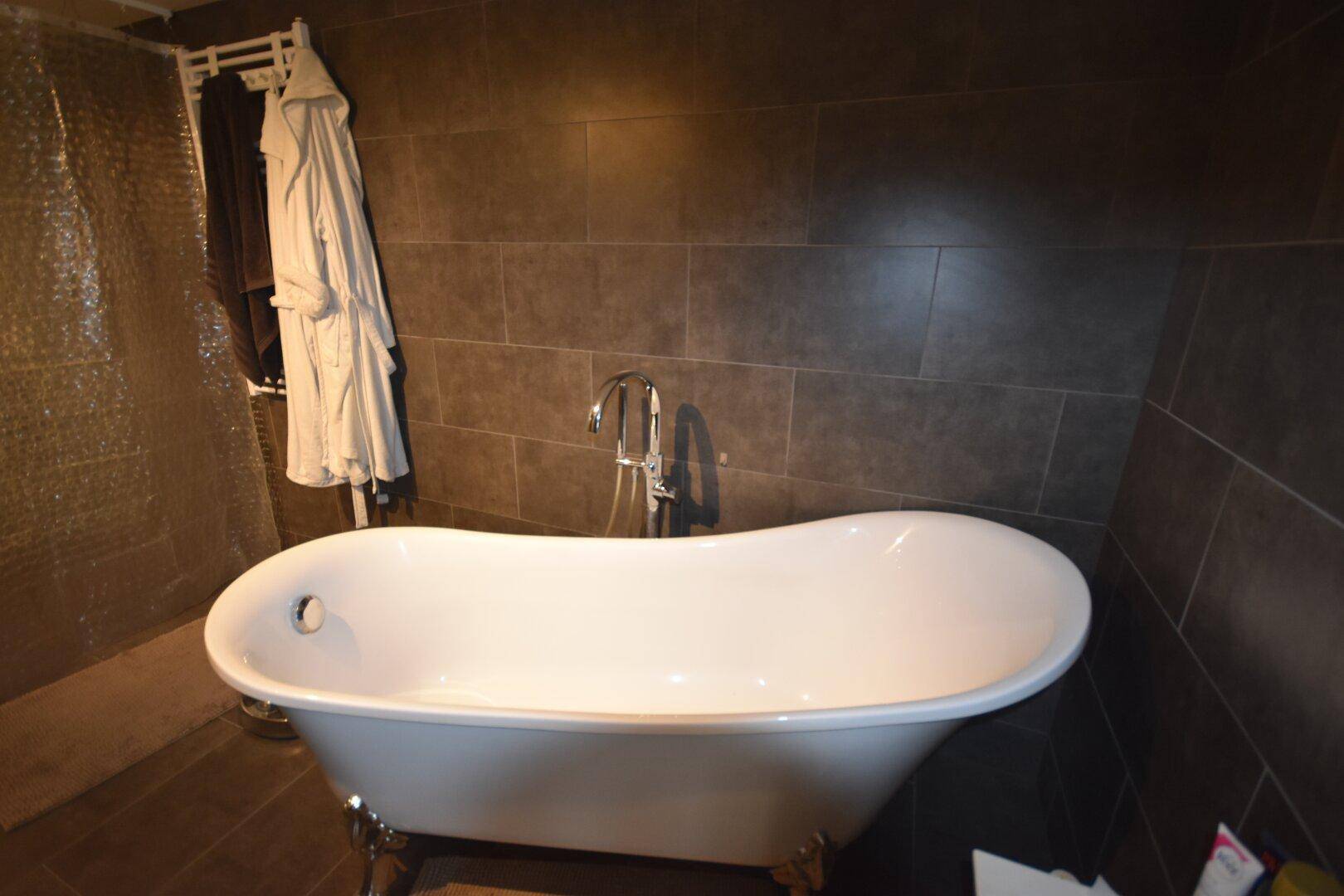 Freistehende Badewanne in einem modern gefliesten Badezimmer mit dunklen Wandfliesen.