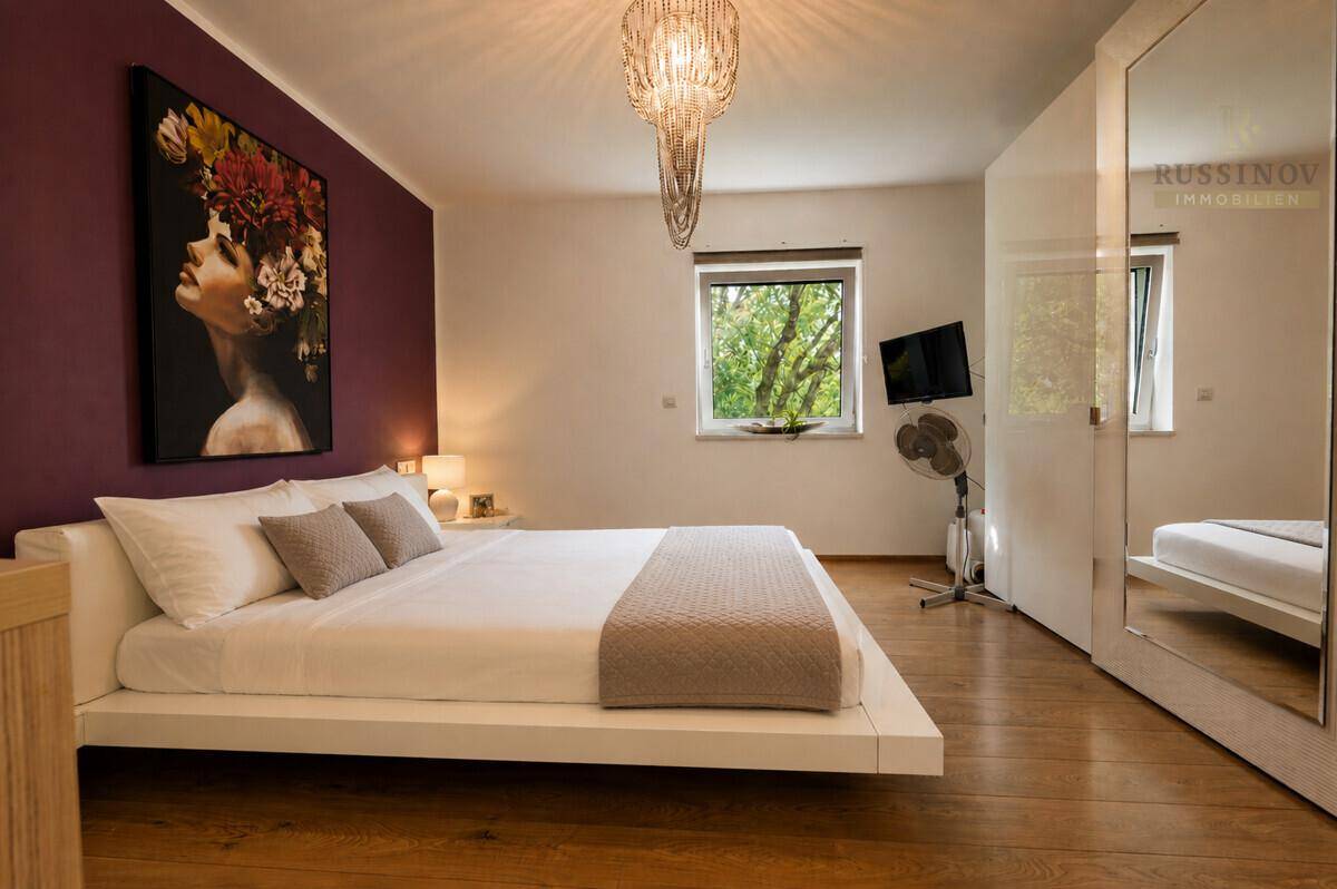 Gemütliches Schlafzimmer mit modernem Bett, farbiger Akzentwand und warmem Holzboden.