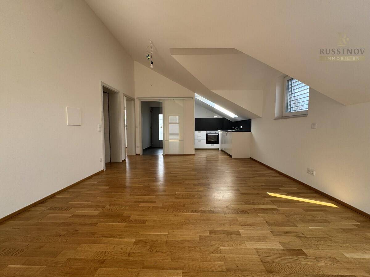Offener Wohnbereich im Dachgeschoss mit Holzboden und integrierter Küchenzeile unter der Dachschräge.