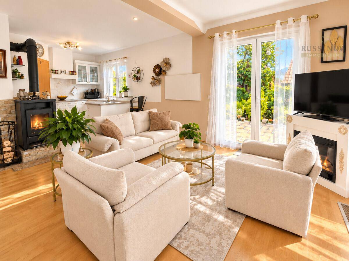Heller offener Wohnbereich mit Kaminofen, beigen Sofas und Zugang zum Garten.
