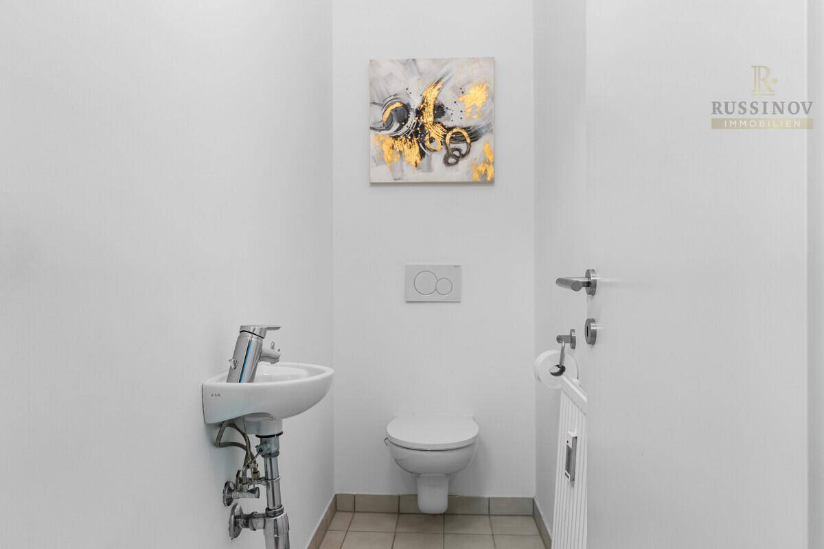 Kleines Gäste-WC mit wandhängender Toilette und modernem Waschbecken, hell gefliest.