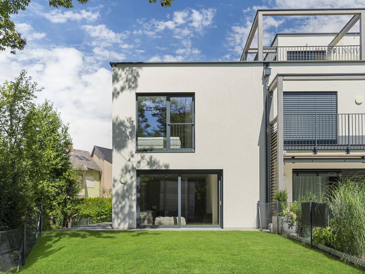 Moderne Gebäudefassade mit großen Fenstern und Zugang zum Gartenbereich.