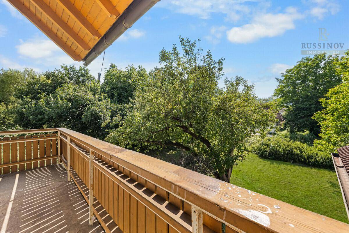 Blick vom Holzbalkon auf die umliegende grüne Landschaft und Bäume.