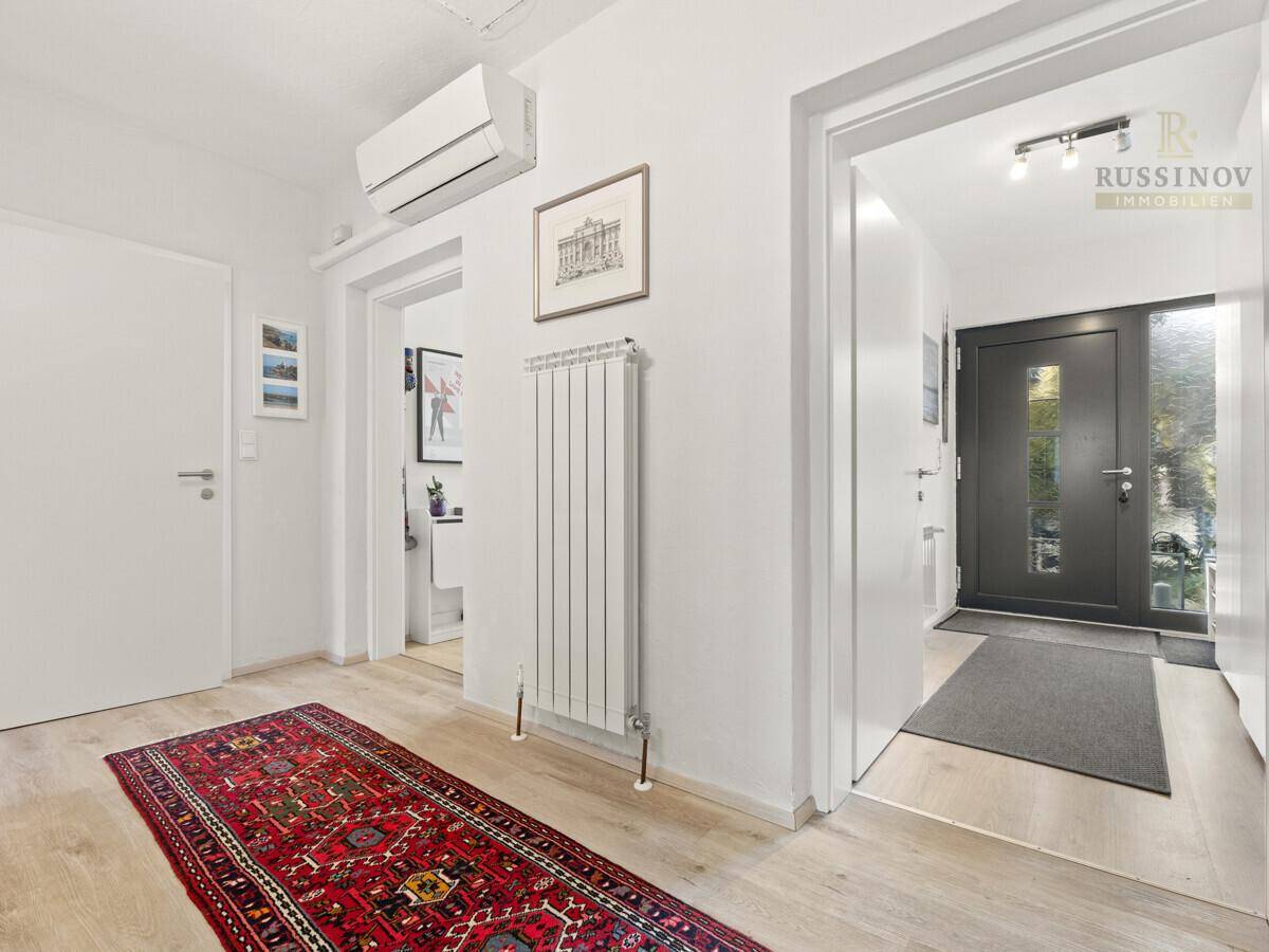 Heller Flur mit Holzboden, Heizkörper und Klimaanlage, führt zum Eingangsbereich.