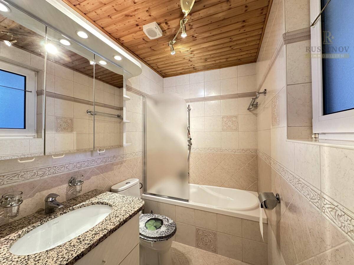 Gefliestes Badezimmer mit Badewanne, Duschabtrennung und Holzdecke.