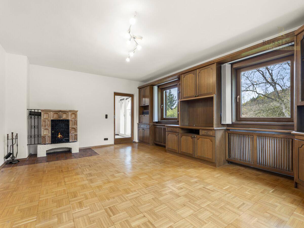 Gemütliches Wohnzimmer mit Parkettboden, einem traditionellen Kachelofen und Holzmöbeln.