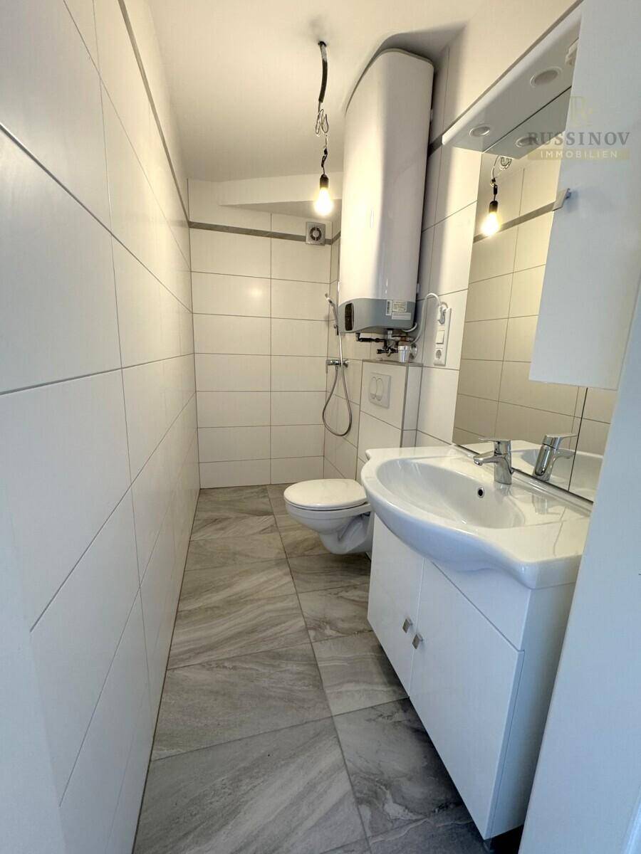 Schmales Badezimmer mit weißen Wandfliesen, modernem Waschtisch und wandhängendem WC.
