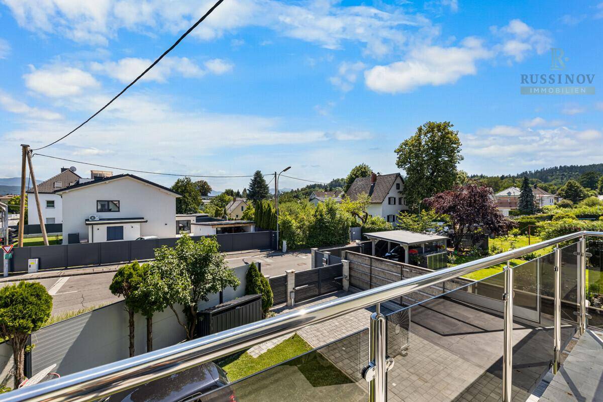 Ausblick vom Balkon auf die Nachbarschaft mit Häusern und grünen Hügeln im Hintergrund.