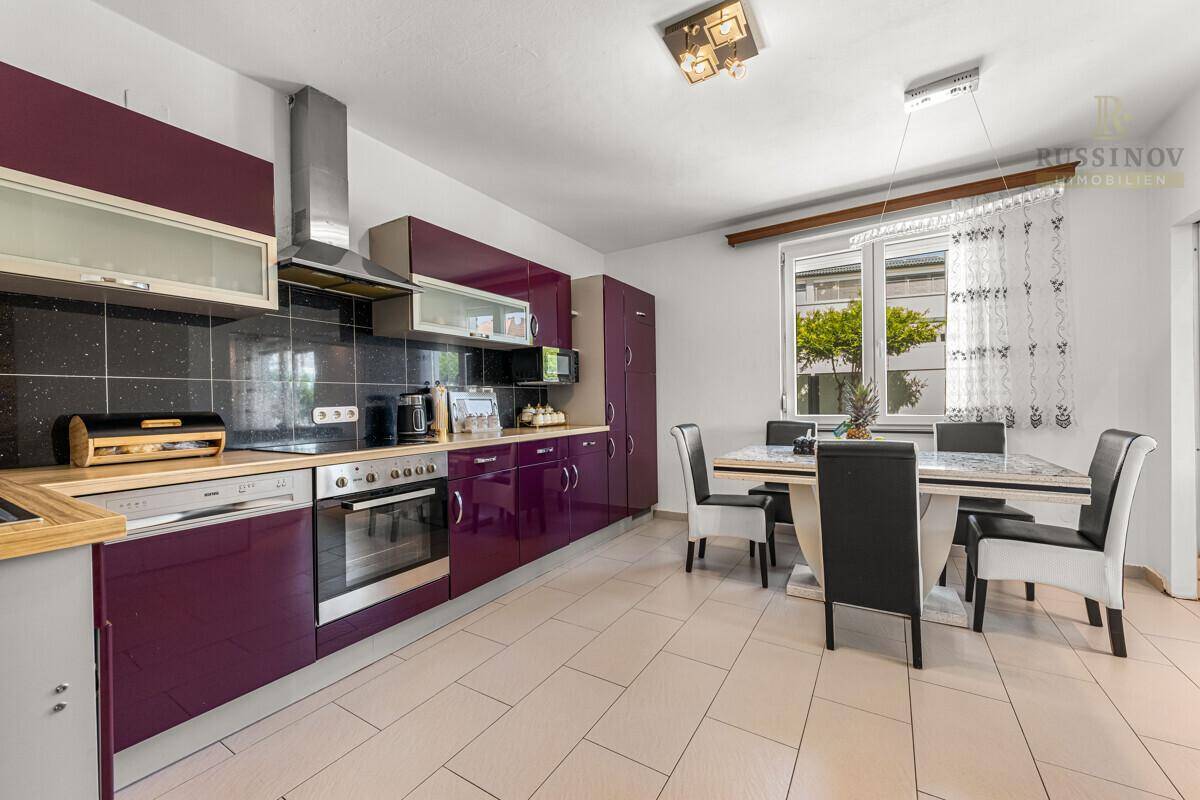 Geräumige Küche mit lila Schränken, Essbereich und Fenster für natürliches Licht.