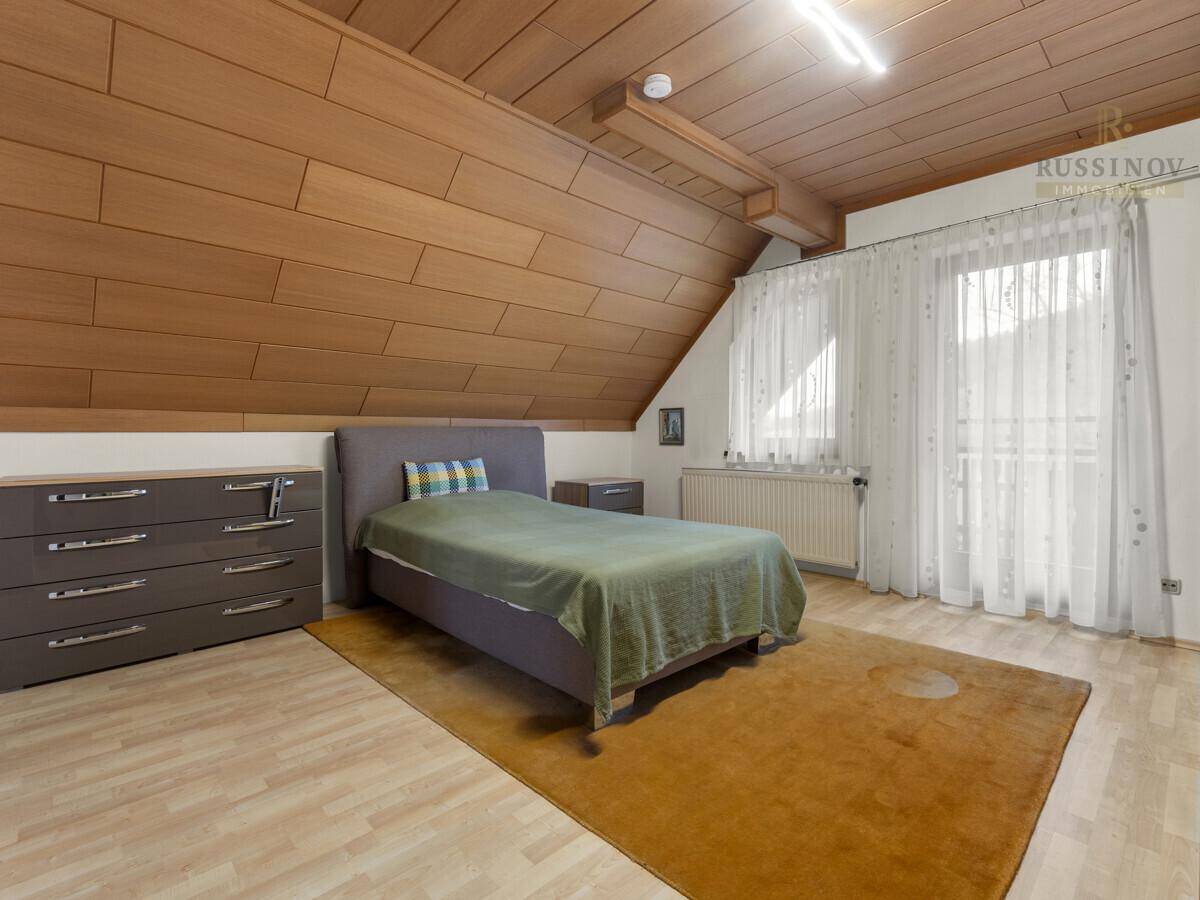 Schlafzimmer mit Holzdachschräge, Laminatboden und Zugang zum Balkon.