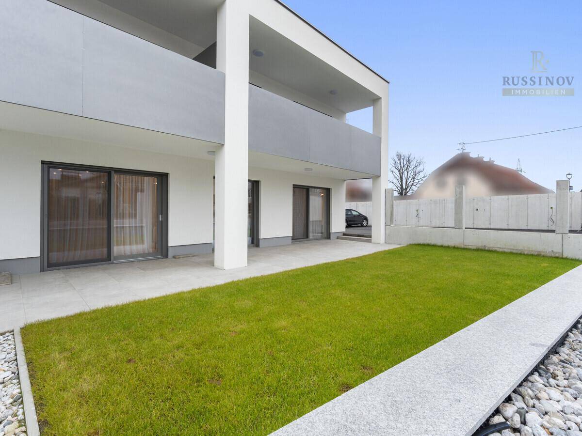 Moderne Gebäudefassade mit privatem Gartenbereich und gepflasterter Terrasse im Erdgeschoss.