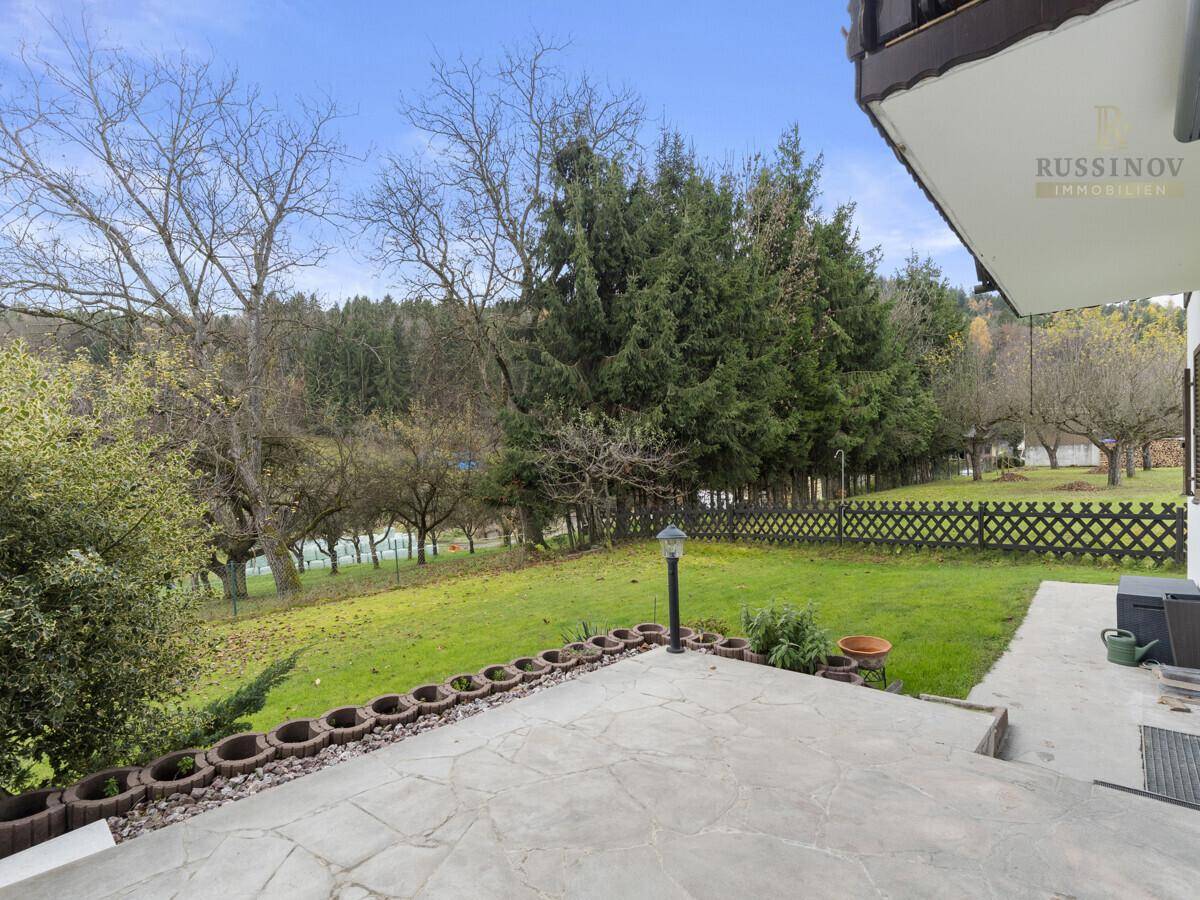 Gepflasterte Terrasse mit Blick auf einen weitläufigen Garten und alte Bäume in ländlicher Umgebung.