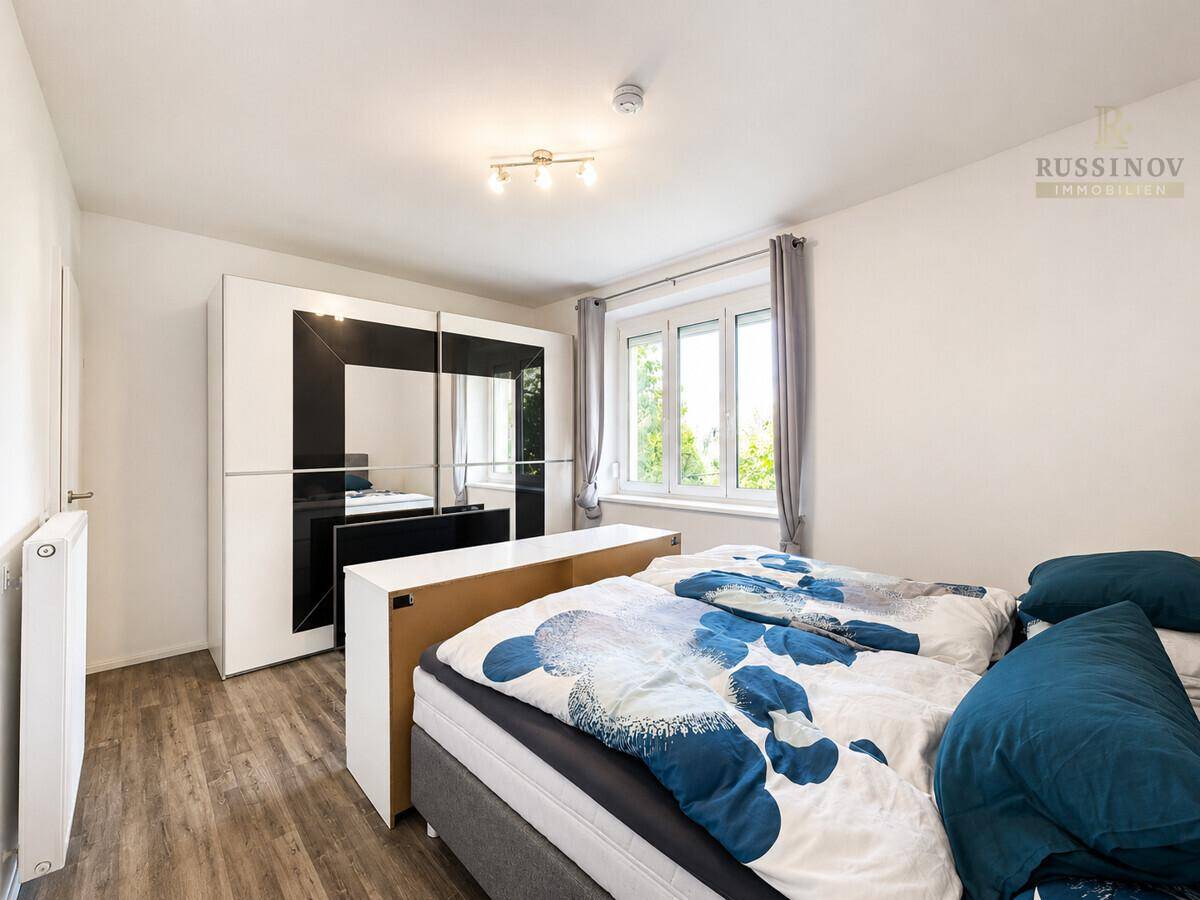 Schlafzimmer mit großem Schiebetürenschrank, Doppelbett und Laminatboden.