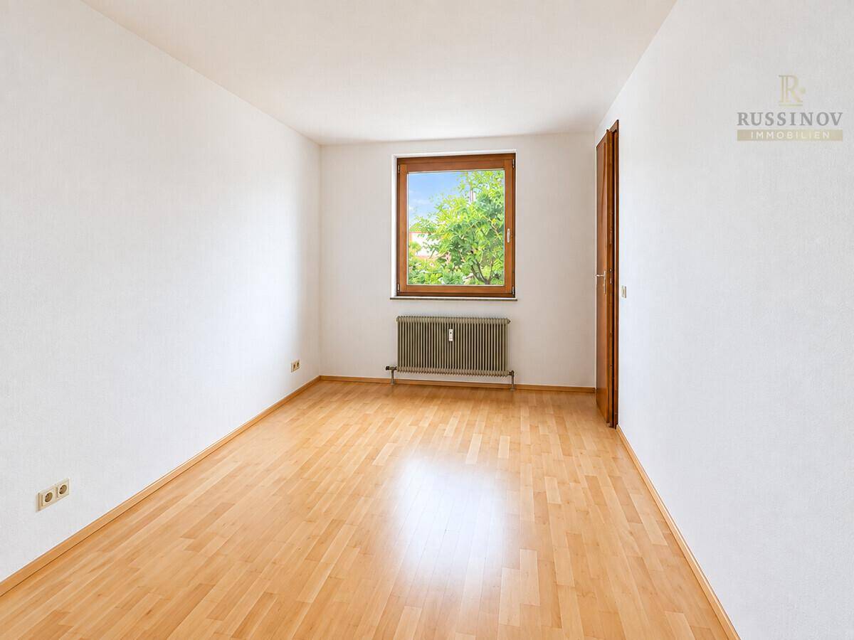 Helles Schlafzimmer mit hellem Parkettboden und Blick ins Grüne durch das Fenster.