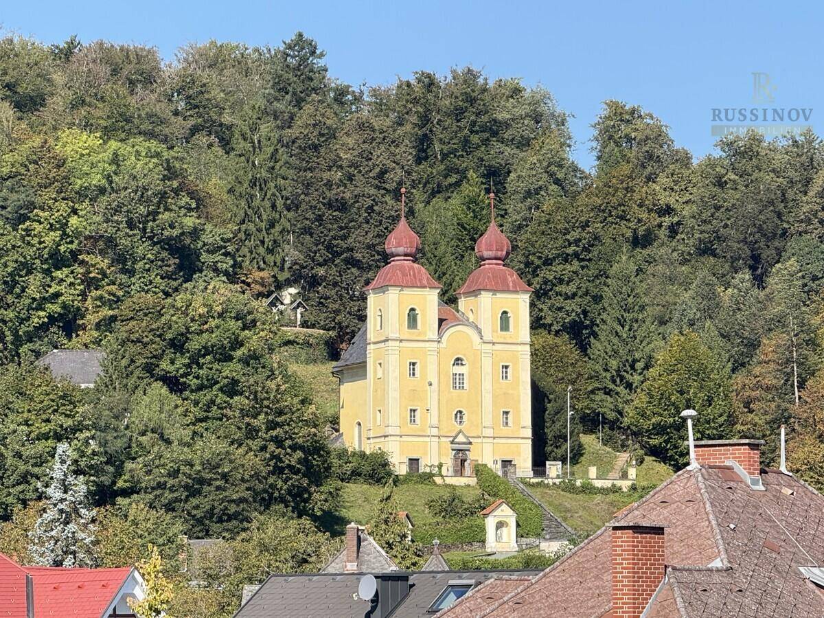 Historische gelbe Kirche mit roten Kuppeln auf einem bewaldeten Hügel.