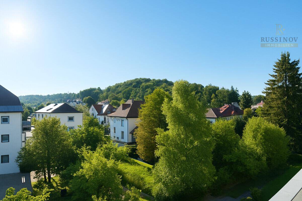 Weitläufiger Blick über eine grüne Hügellandschaft mit Wohnbebauung und Bäumen.