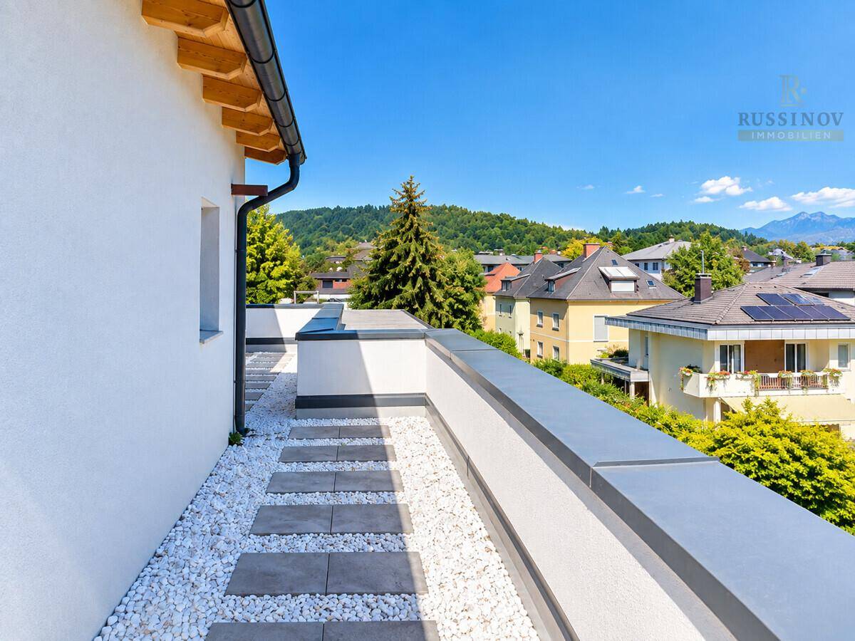 Moderne Dachterrasse mit Kies und Trittplatten, umgeben von grüner Landschaft und Häusern.