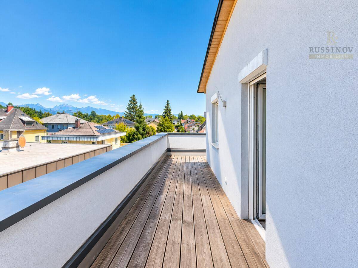 Geräumige Holzterrasse mit weitem Blick über die Dächer und die umliegende Berglandschaft.