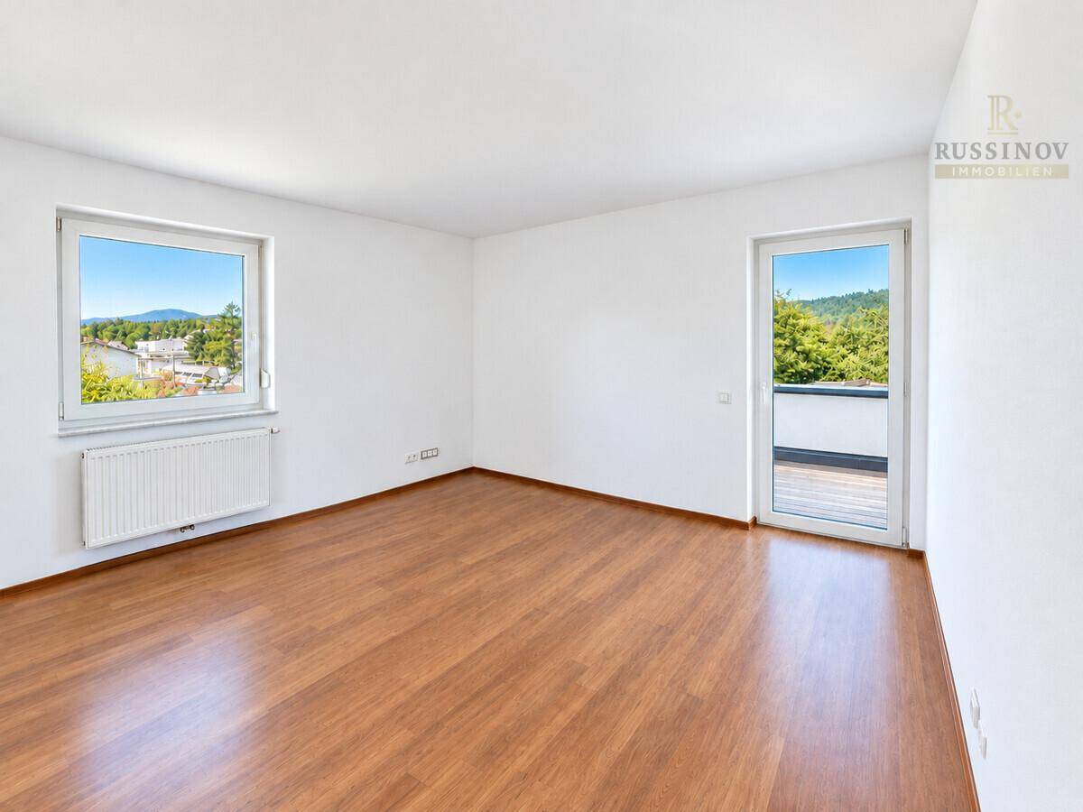 Helles Schlafzimmer mit Laminatboden und direktem Zugang zu einem Außenbereich mit grüner Aussicht.