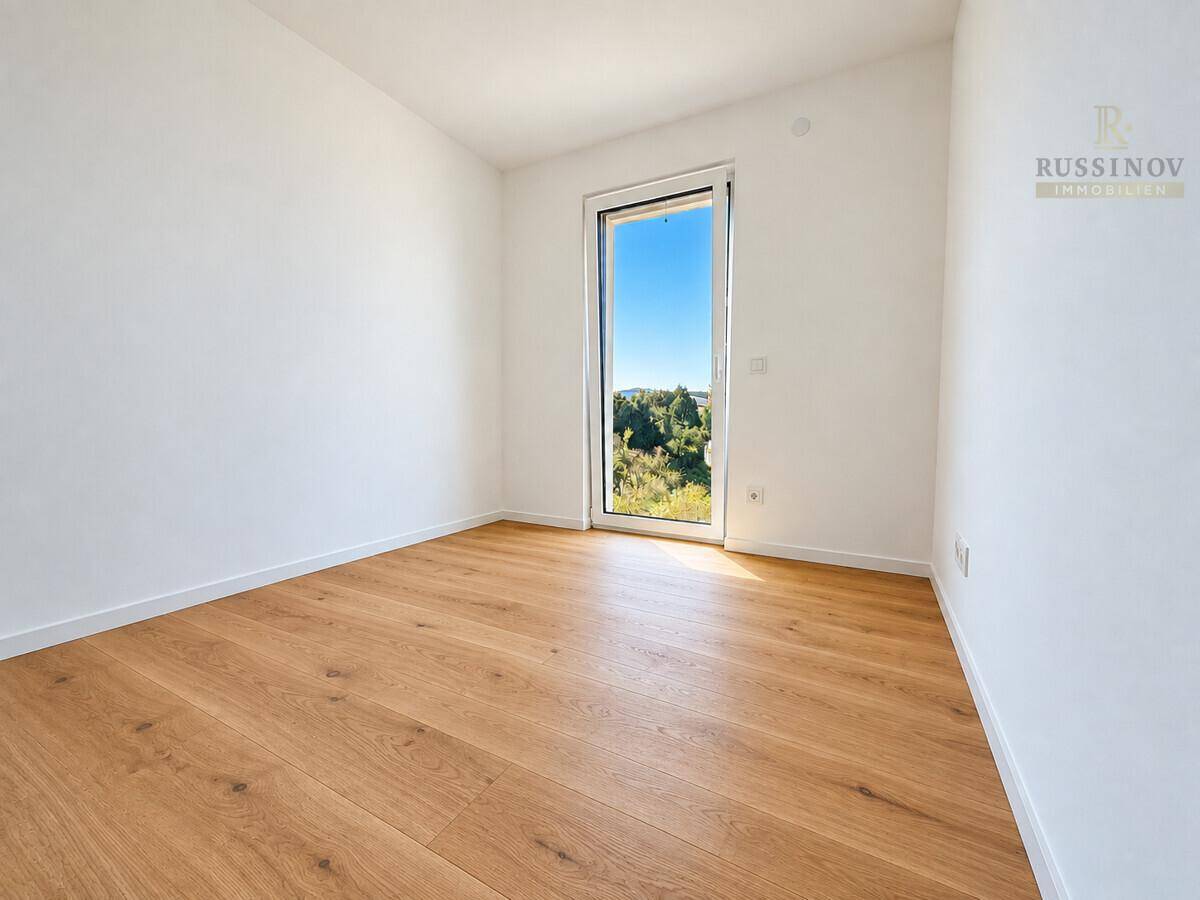 Helles Schlafzimmer mit Holzboden und einem Fenster mit Blick ins Grüne.