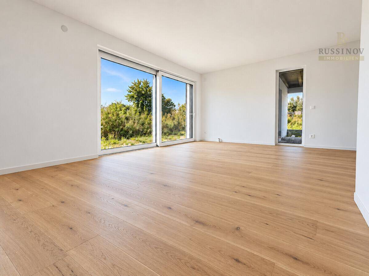 Helles, leeres Wohnzimmer mit großen Schiebetüren und Blick ins Grüne.